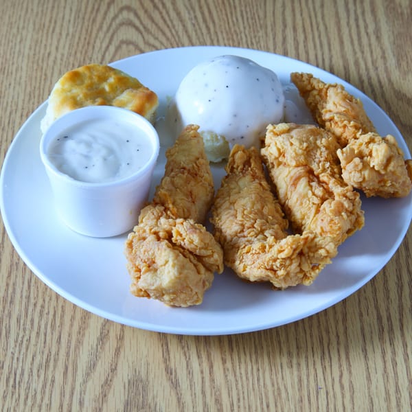Crispy fried chicken tenders, a biscuit, and mashed potatoes with gravy on a white plate.