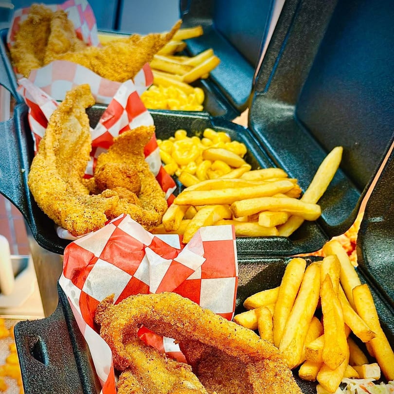 Three takeout containers filled with fried fish, french fries, and macaroni and cheese.