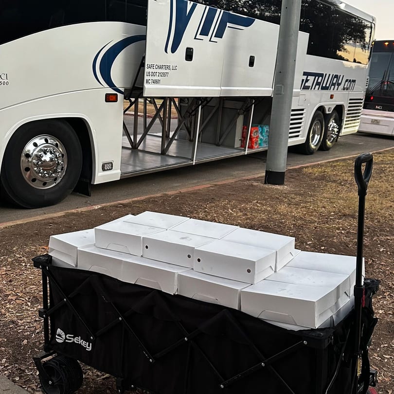 A black wagon filled with white boxes sits in front of a white charter bus with open storage.