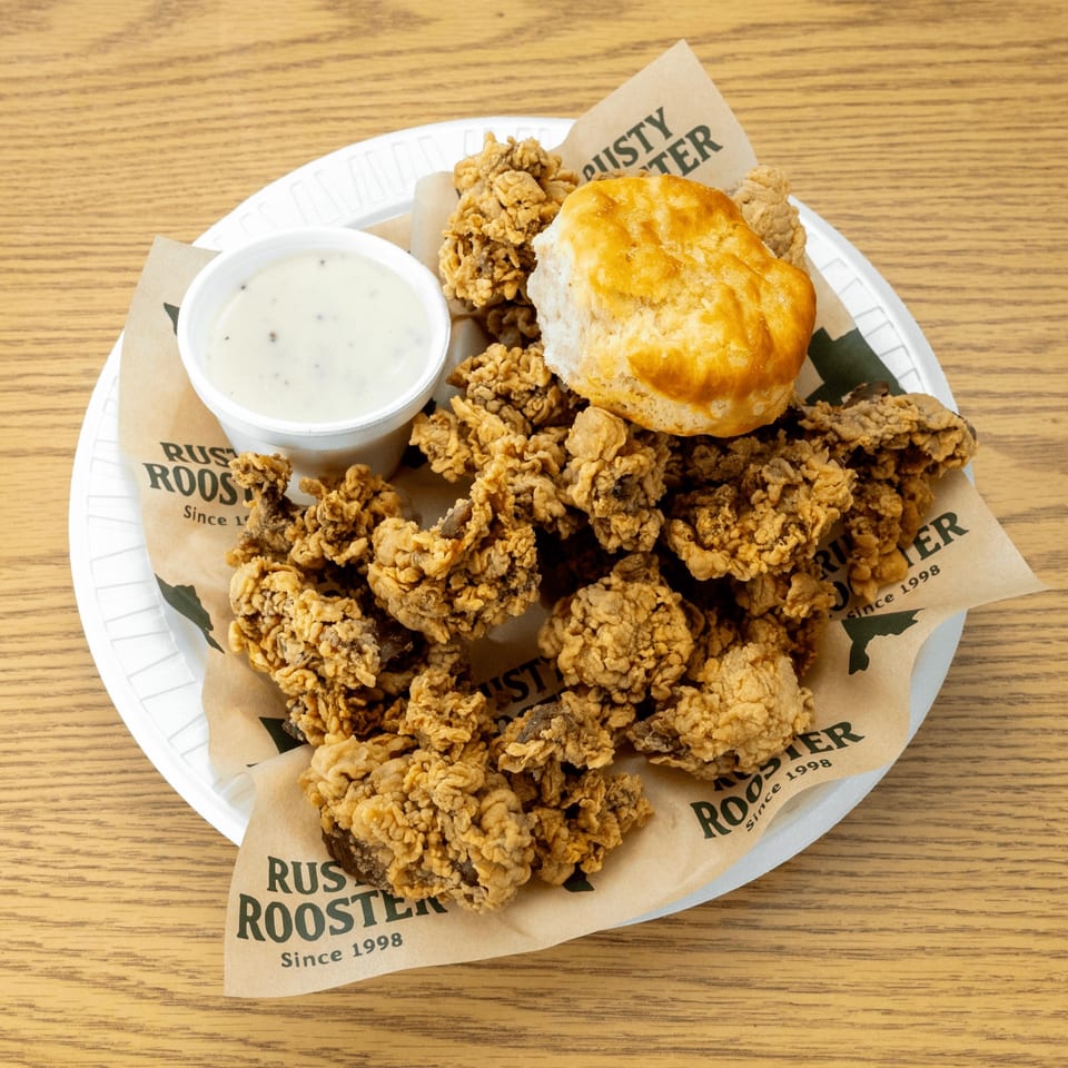 Crispy fried chicken livers with a biscuit and gravy on a Rusty Rooster branded paper liner.