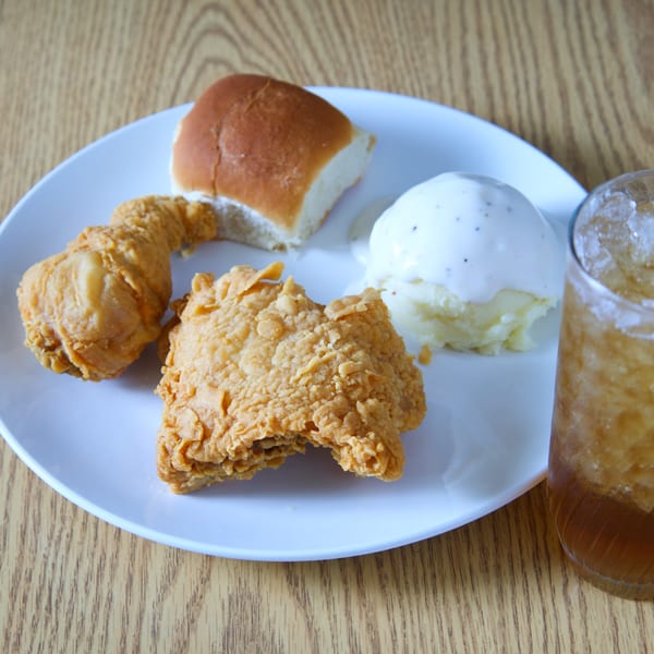 Fried chicken pieces, mashed potatoes with gravy, a dinner roll, and an iced drink on a white plate.