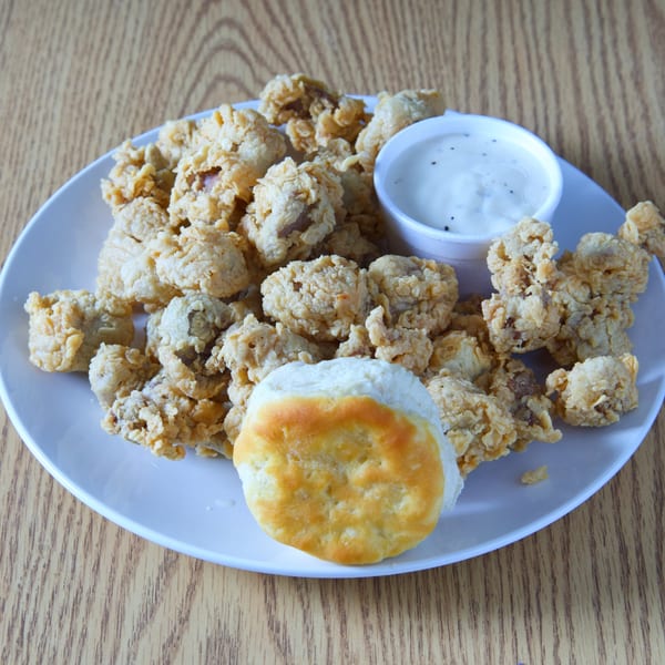 Fried chicken gizzards with a biscuit and a side of white gravy on a white plate.