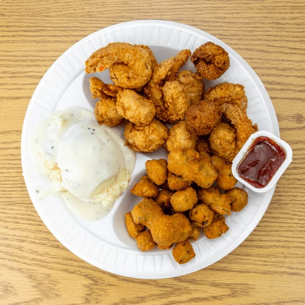 Fried shrimp, fried okra, and mashed potatoes with gravy on a white segmented plate.
