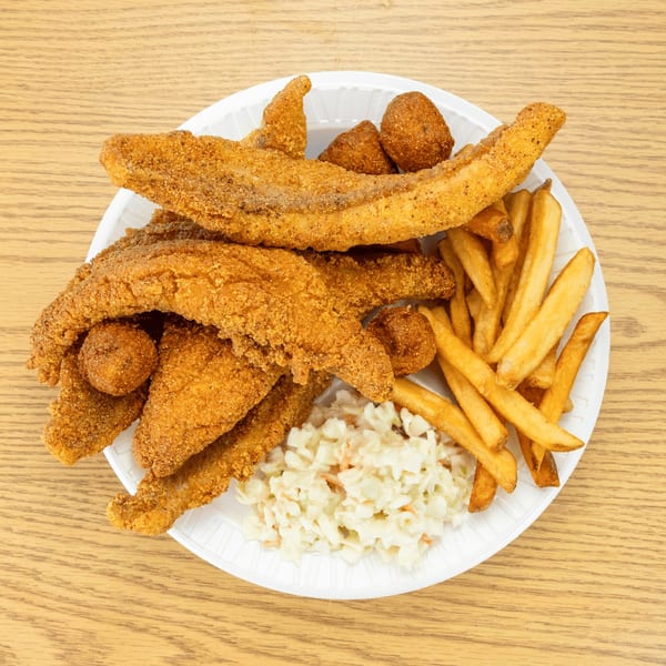 Fried fish fillets, hush puppies, french fries, and coleslaw on a white paper plate.