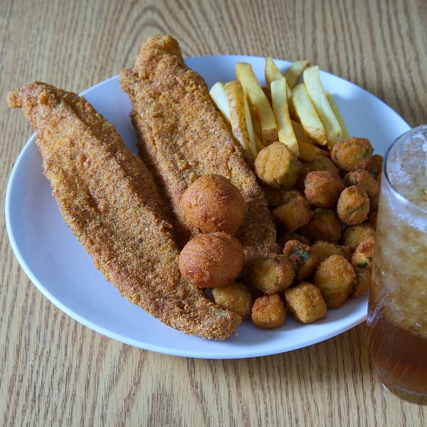 Fried fish fillets, hush puppies, french fries, and fried okra on a white plate with a drink.