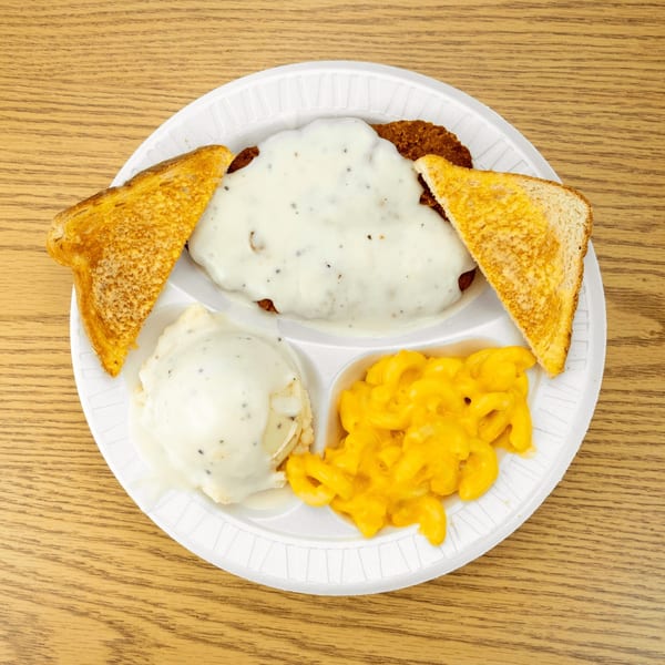 A chicken fried steak with gravy, mashed potatoes, mac and cheese, and toast on a white plate.