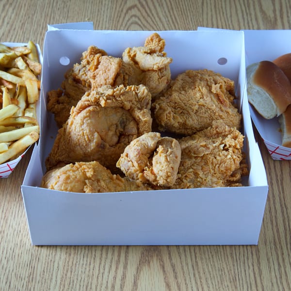 Fried chicken pieces in a white box, with fries and dinner rolls in separate containers.