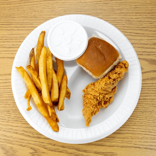 A fried chicken tender, french fries, a dinner roll, and a covered sauce cup on a white plate.